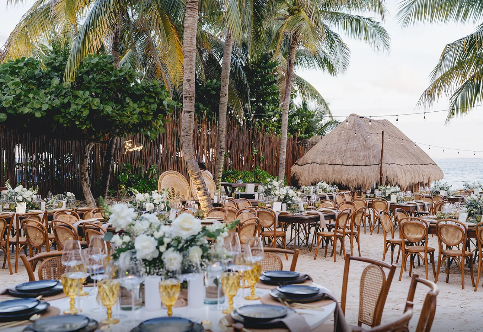 Elegant beachfront social event with white florals and thatched roof