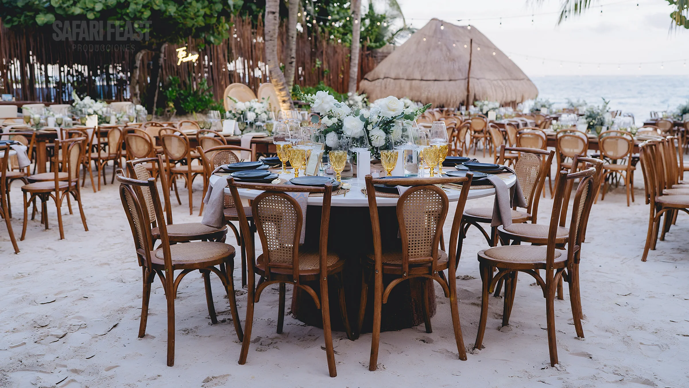 Beachfront destination wedding reception on the sand with cross-back chairs and white floral centerpieces in the Riviera Maya